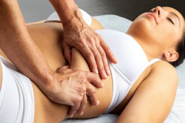 Close up of hands applying pressure with thumbs under woman's thorax. Girl having abdominal physiotherapy in spa. clipart