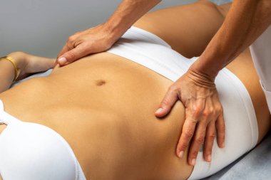 Kadın karnını manipüle eden fizyoterapist. Terapisti kalçalarına baskı yapan bir kız spa yatağında yatıyor..