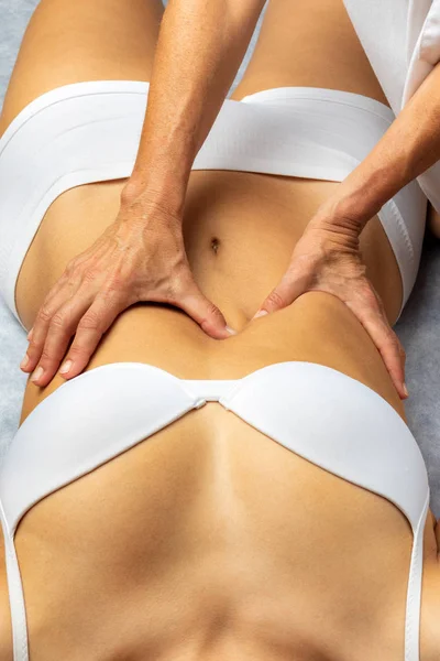 Top view of physiotherapist applying pressure on female stomach. Hands massaging abdomen releasing intestinal obstruction.