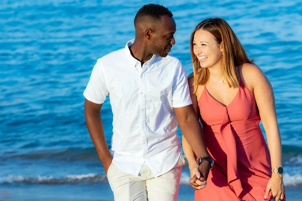 身着休闲装的年轻夫妇手牵手在海滩上的特写 蓝海背景下的非洲男人和高加索女人 — 图库照片