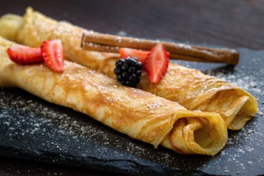 Koyu fayanslı ince fırınlanmış krepleri tarçın ve kırmızı meyvelerle kapatın..