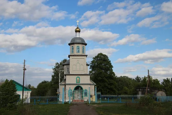 Spring landscape with a rural church under a blue sky with white clouds in the village of Ukhmany — Stock Photo, Image