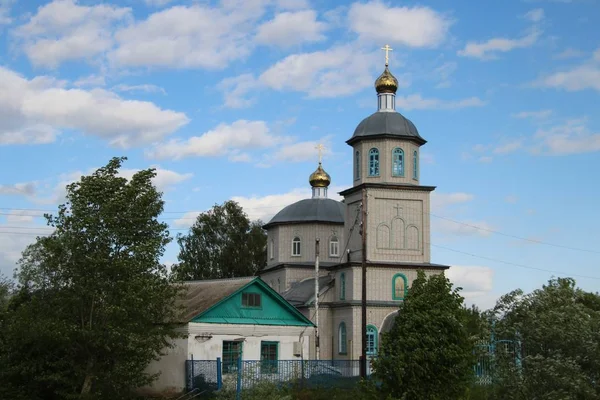 Lente landschap met een landelijke kerk onder een blauwe hemel met witte wolken in het dorp Ukhmany — Stockfoto