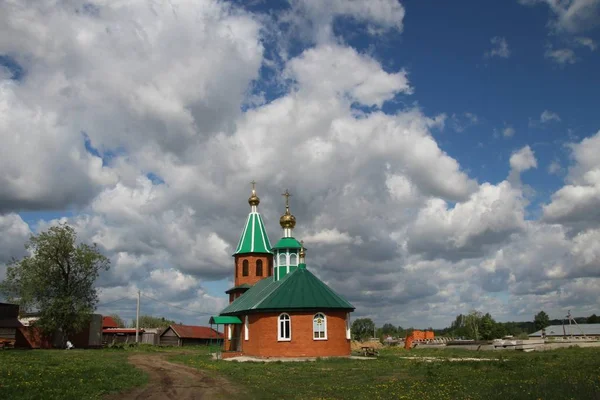 Landschap met uitzicht op een landelijke kerk onder een blauwe hemel met witte wolken in Chuvashia — Stockfoto