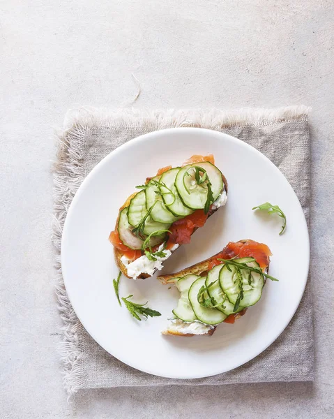 Salmon, cucumber and cream cheese rye sandwich on the wooden background, top view. Delicious snack or appetizer for wine.