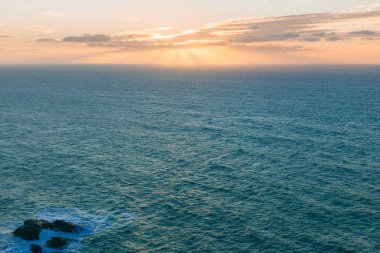 akşam güneşi bulutların ve ufka uzanan mavi okyanus arkasında