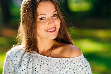 Genç kız kamera lensi ve gülümsüyor Açıkçası üzerinde arka planı yeşil bulanık görünüyor