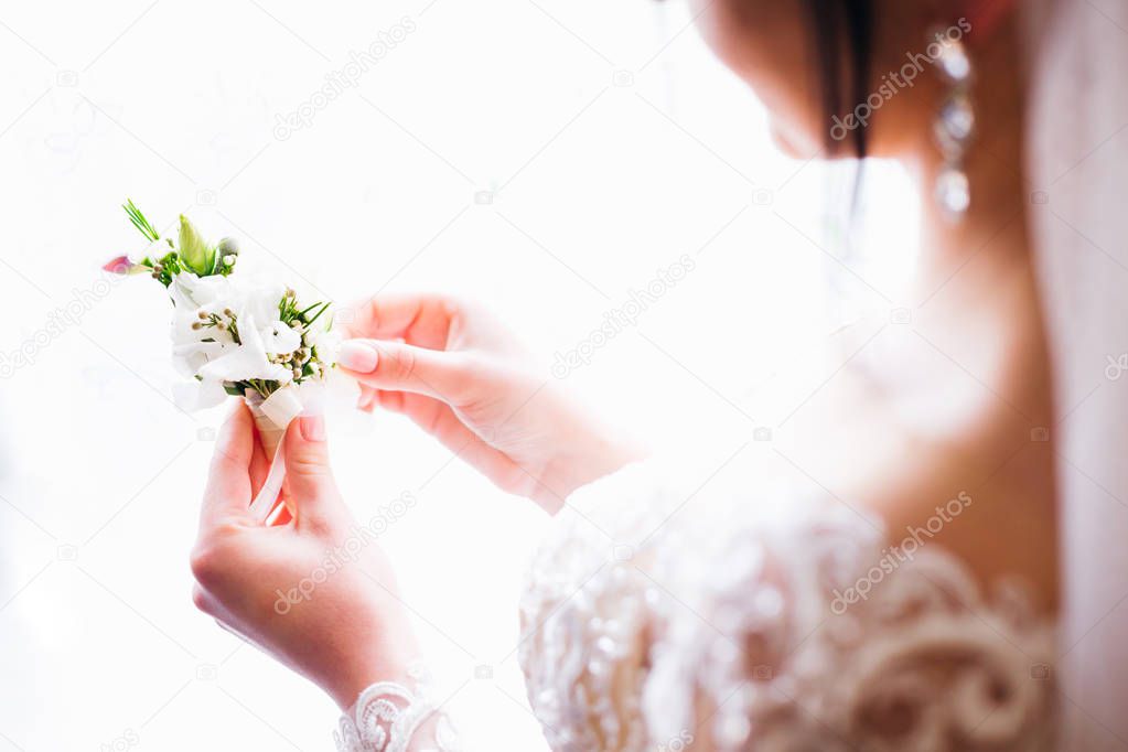 The bride admires a beautiful bouquet for the groom to will fix on his jacket