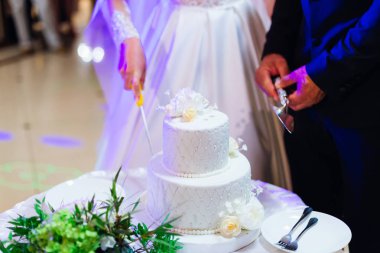 Yeni evliler güzel ve beyaz bir düğün pastası kestiler. Yuvarlak bir masada çok katlı düğün pastası