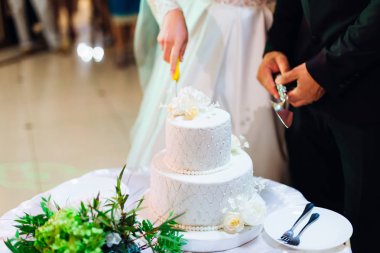 Yuvarlak bir masada çok katlı düğün pastası. Yeni evliler bir tanesinin yanında duruyor ve düğün pastası kesiyorlar.
