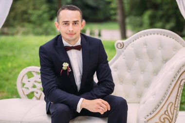 Mutlu damat lüks beyaz bir kanepede oturur ve kamera lensine bakar..