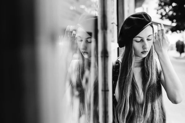 a dreamed girl in a black cap fixes her long hair with her hand on a black and white photo