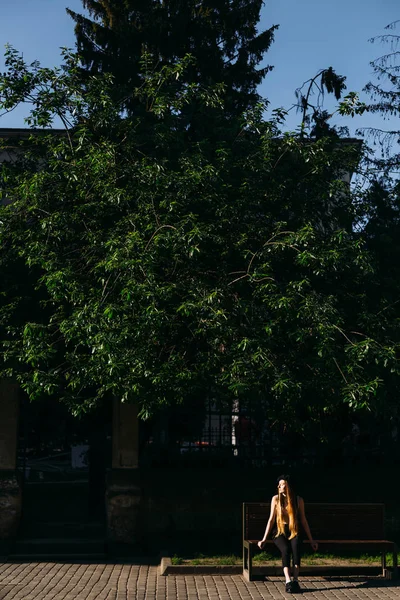 Νεαρό Κορίτσι Που Κάθεται Ένα Παγκάκι Κάτω Από Ένα Δέντρο — Φωτογραφία Αρχείου