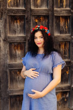 Müstakbel genç anne, ahşap bir kapının arkasında göbeğinin üstünde el ele tutuşuyor.