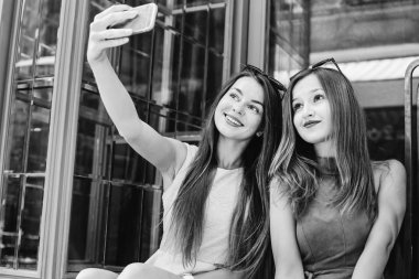 Kafalarında güneş gözlüğü olan tatlı kızlar siyah beyaz bir fotoğrafta cam kapıların arkasında selfie çekiyorlar.