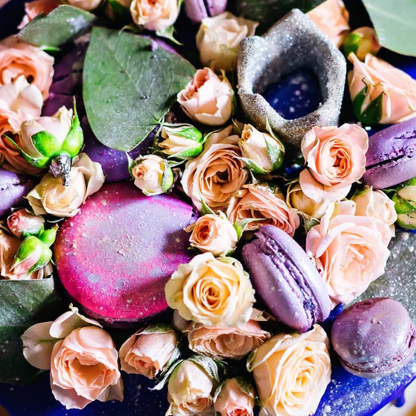 Pastanın tepesine alışılmadık dekorasyonlarla yakın plan. Yeşil yapraklı narin güller ve badem kurabiyeleri