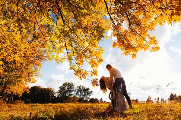秋の草原の背景に彼女の背を曲げた彼の最愛の妻をサポートしています — ストック写真