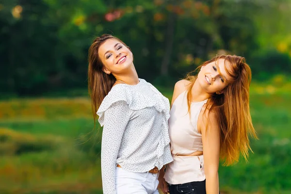 güzel kızlar kamera objektifi çim ve ağaçların arka plan bakarak. güzel gülümsüyor ve yan yana duran hafif makyaj kızlar