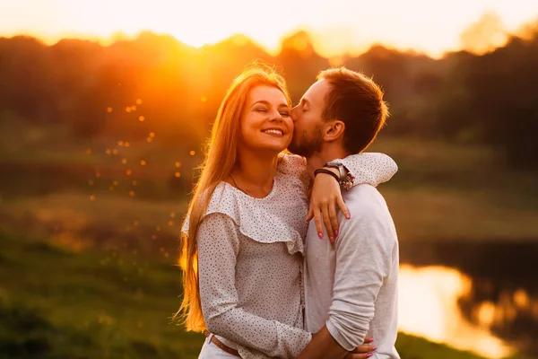 ひげの男は優しく頬に彼のガール フレンドをキス 彼女はそれを楽しんでいます 夕日の背景に穏やかな抱擁 — ストック写真