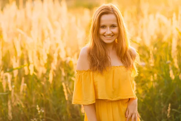 a beautiful girl in a stylish dress laughing and looking into the camera lens on a field with high grass