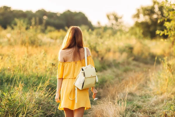 Girl goes to the field and she inverted back to the camera and backpack on her shoulders