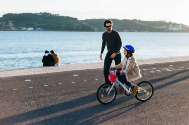 Lisbon, Portekiz - Ocak 2018 baba oğluyla nehir kıyısında bisiklete binen bir kaykay üzerinde