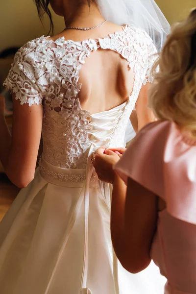 bride\'s girlfriend helps the bride dress up her wedding dress