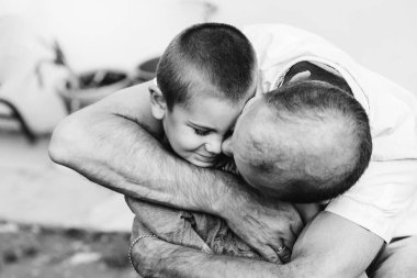 an uncle gently hugs and kisses his little nephew in the cheek on black and white photography clipart