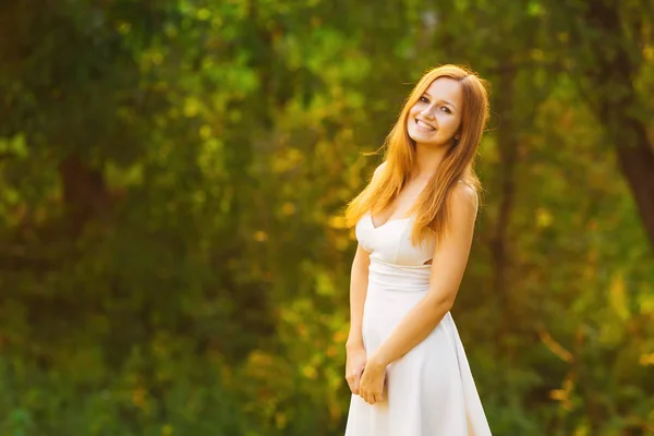 木の背景で白いドレスを着た美しい少女の白い笑顔 — ストック写真