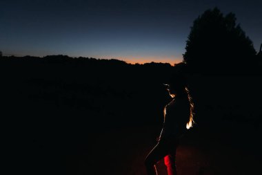 Kız yapay ışık önünde duruyor ve de onu siluet arka planda doğa tarafından konturlu