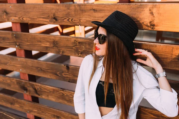 zarif poz ahşap bir çit üzerinde eğilir bir kız. kız şık giysiler ve güneş gözlüğü