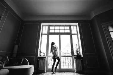 Pencerenin yanında beyaz sabahlık giymiş güzel bir kadın. Siyah beyaz fotoğraf.