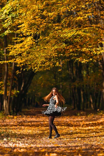 幸せで陽気な美しい若い女性の素敵なドレスでダンスと髪を飛んで 黄色い葉の背景で笑顔で周りの回転の肖像画 秋の公園で散歩します — ストック写真