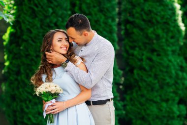 Adam kız arkadaşını öpmek istiyor. Kız güzel bir elbise şık bir buket çiçek yeşil ağaçlar arka plan üzerinde tutar.