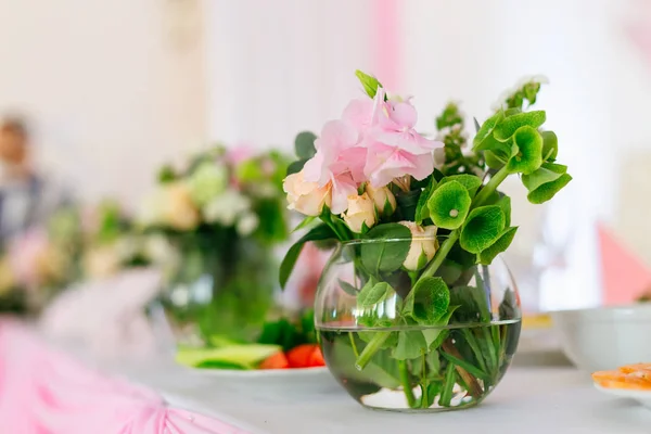 a transparent vase with water in which beautiful flowers with green twigs on a festive table