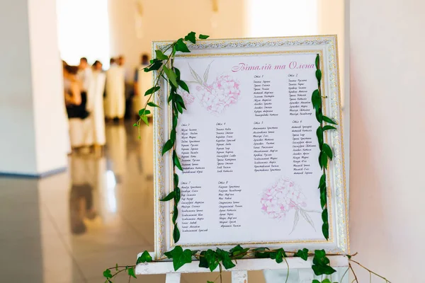 a list of guests on a wooden board which is on the easel in the restaurant hall