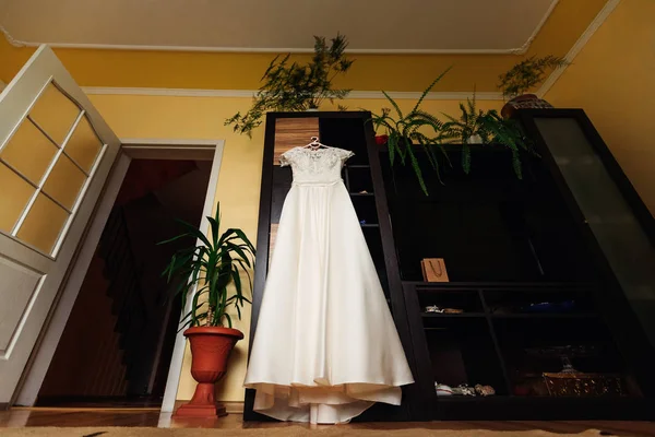 a wedding dress on a hanger on a door closet. beautiful living room interior and wedding preparation