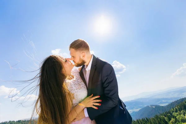 groom want to kiss the bride and hug her waist against the background of the mountains and the blue sky