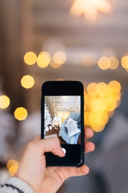 el bir adam akıllı telefon tutar ve rahat bir oda Noel süslemeleri ile fotoğrafını çekin