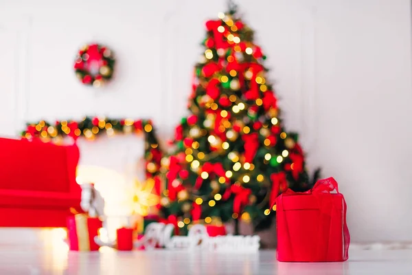 red box with a ribbon on the background of a room with a blurred Christmas tree, a sofa and a fireplace