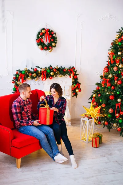 Menina Entusiasticamente Abre Presente Natal Enquanto Sentado Sofá Vermelho Seu — Fotografia de Stock