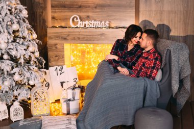 Adam ve kız yüz yüze yumuşak bir koltukta oturan ve rahat bir oda bir Noel ağacı ve bir şömine yakın bir yorgan ile kaplıdır