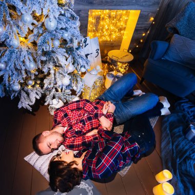 yerde yatarken ve birbirlerine gülümseyerek mutlu bir çift. rahat oda şömine, Noel ağacı, hediyeler ve mum