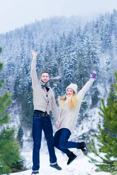 the couple in love hold hands and jump in the mountains against the background of trees that are covered with snow