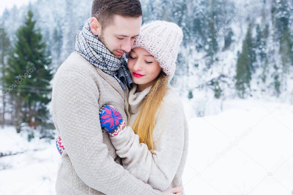 The couple in love in sweaters embrace the backdrop of a mountain covered with forest and snow