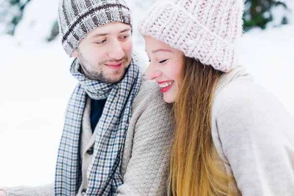 the guy looks at the girl who sincerely smiles and her eyes is closed. they sit on the snow in warm clothes