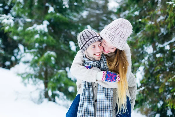 The girl jumped on the back of the guy and they smile against the background of the winter forest