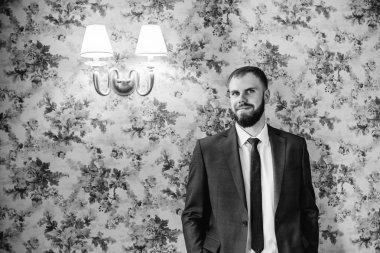 Damat takım elbise gülümsüyor ve duvar ve siyah ve beyaz fotoğraf kamera objektif bakar karşı eğilir