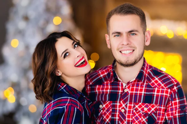 sincere smile of a girl with a beautiful makeup and a guy next to her who also smiles and they look at the camera lens on blurred background with a Christmas theme