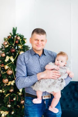 mutlu baba küçük kızı ellerinde tutan ve kamera lensi bir Noel ağacı arka plan üzerinde görünüyor